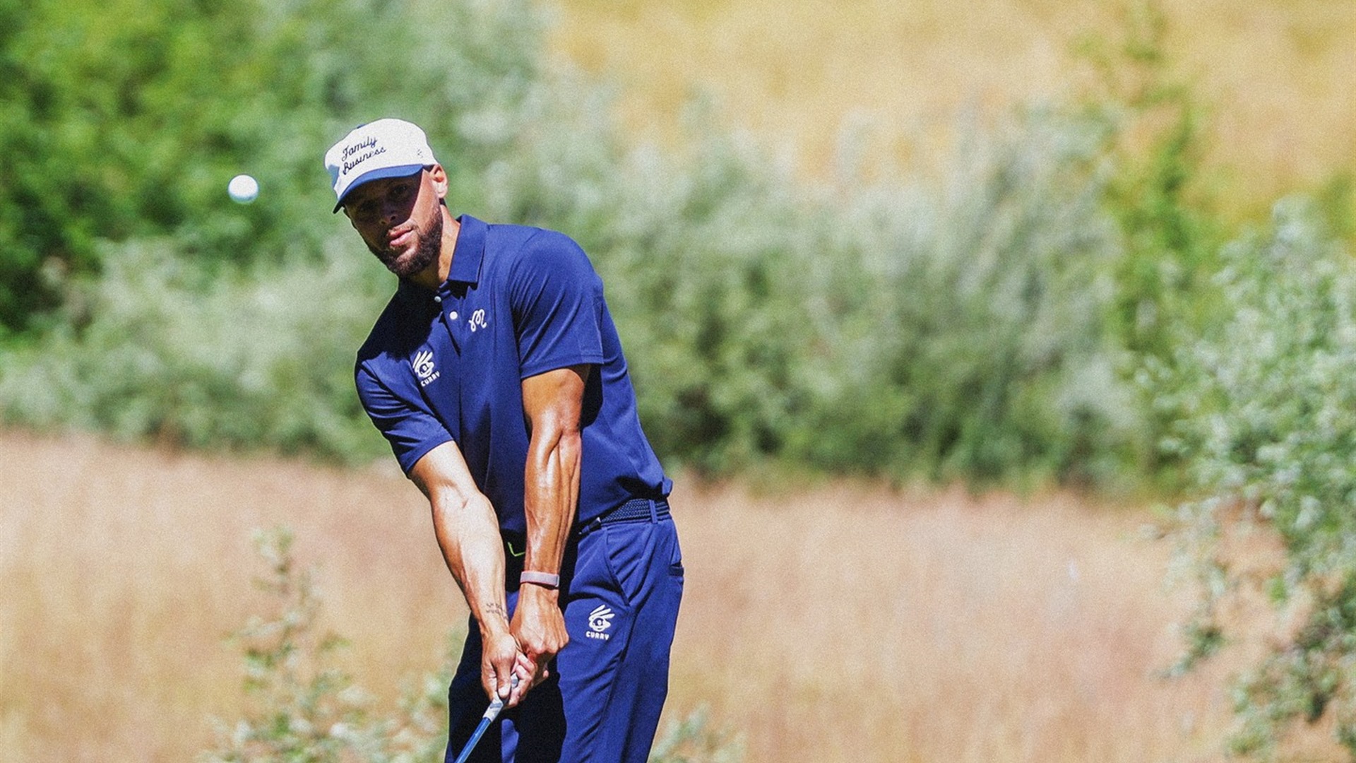 Stephen Curry 穿 Curry Brand × Malbon 聯名海軍藍 Polo 與白色 Family Business 球帽,在球道上切球